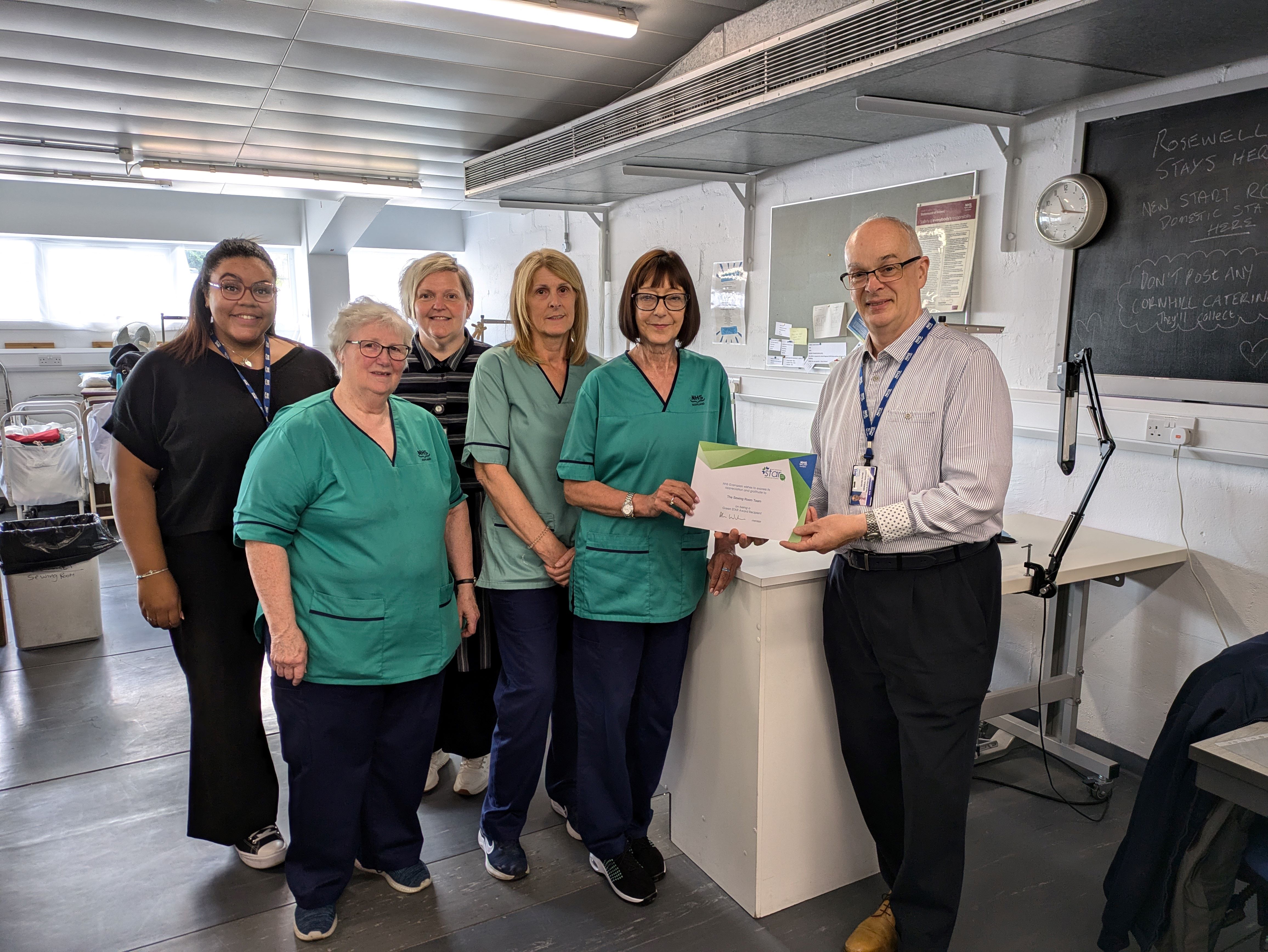 Pictured in the Sewing Room at Foresterhill (from left to right) staff members: Olivia Finnie, Administration Assistant; Maureen Kaczmarek, Supervisor; Lynn Christie, Linen Services Manager; Lesley Hall, Sewing Assistant; Angela Ross, Supervisor; and Gavin Payne, General Manager Facilities & Estates, who presented the team with their award.